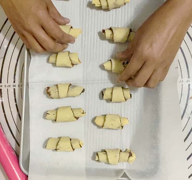 A person placing unbaked rugelach on a baking tray.