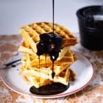 A stack of waffles with chocolate syrup on a plate.