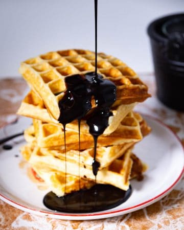 A stack of waffles with chocolate syrup on a plate.
