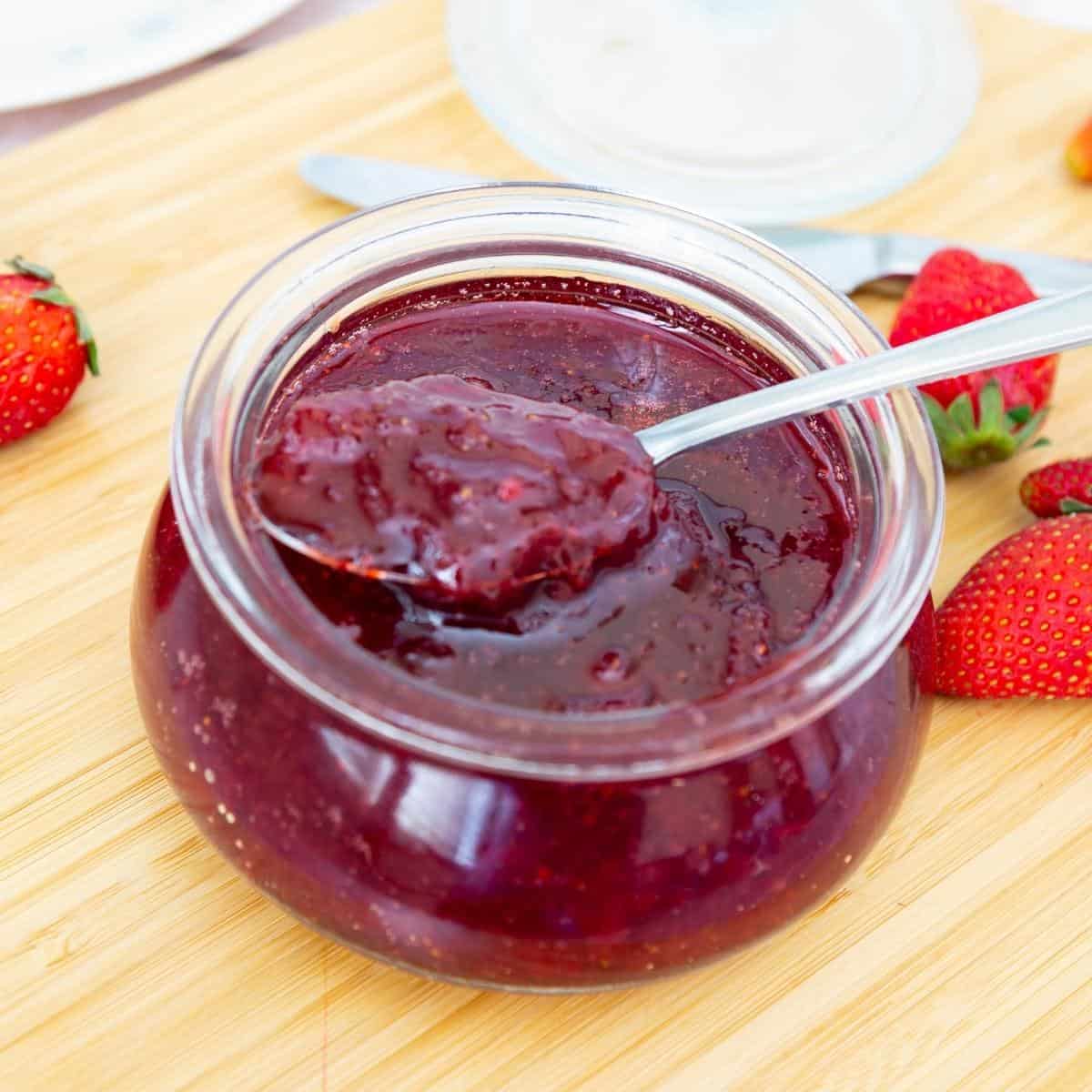A bowl with strawberry jam and a spoon.