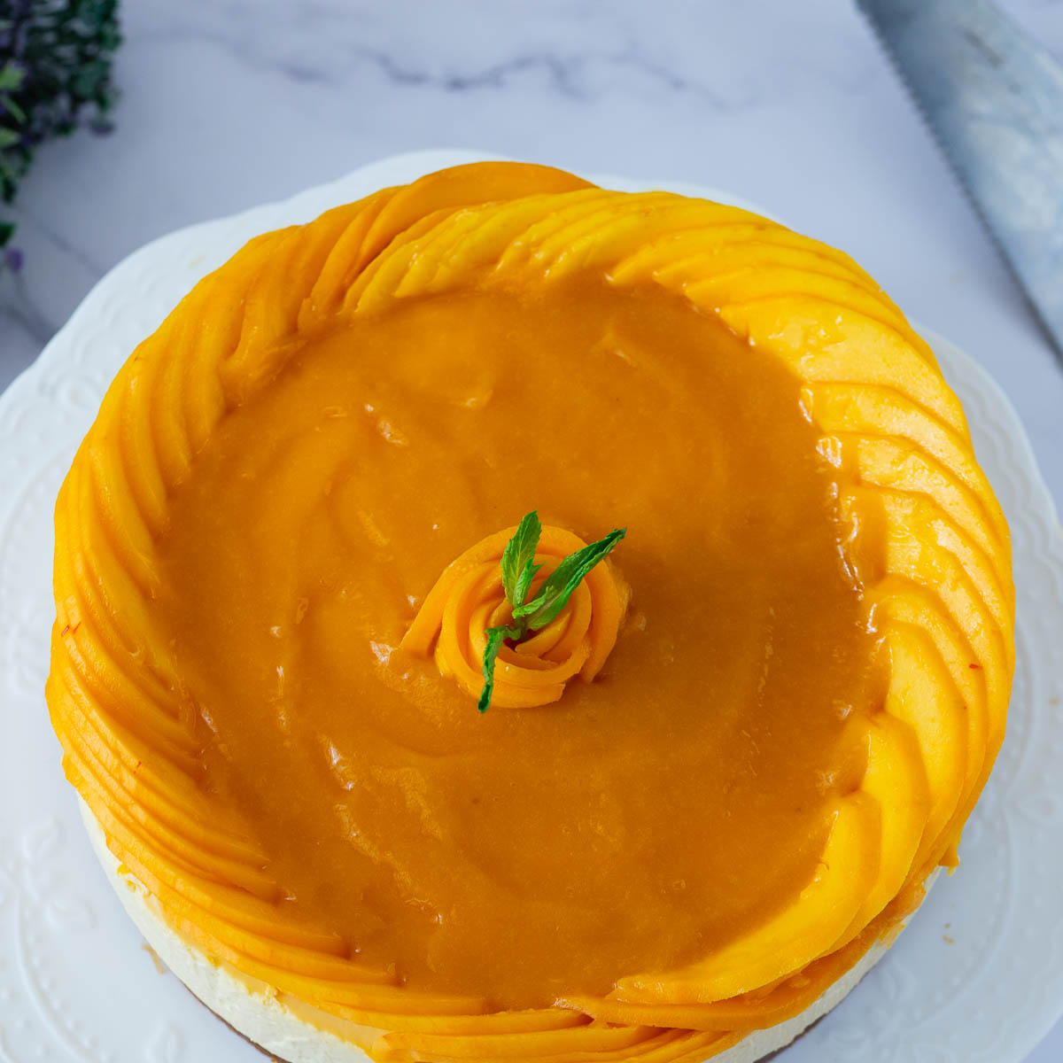 A no bake cheesecake with mango puree and fresh mangoes on the cake stand.