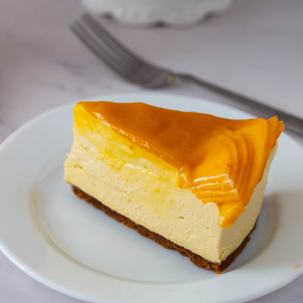 A slice of no bake mango cheesecake with fresh mangoes on the plate.