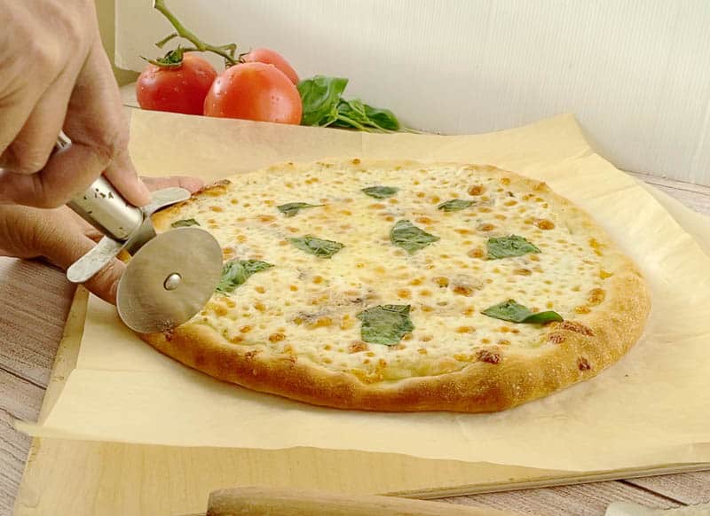 A person slicing a pizza on a wooden board.