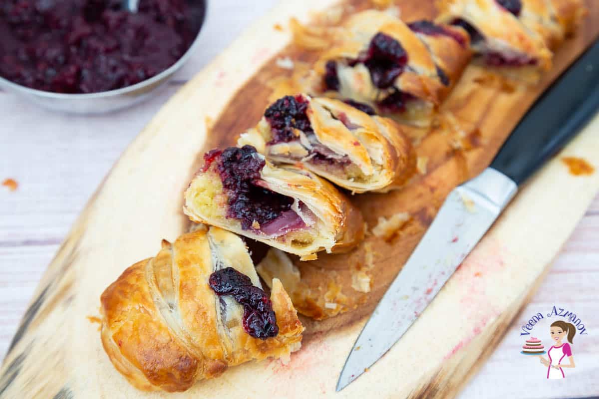 A sliced braided pastry with blackberries on a wooden board.
