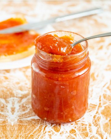 Apricot peach jam in a jar with a spoon.