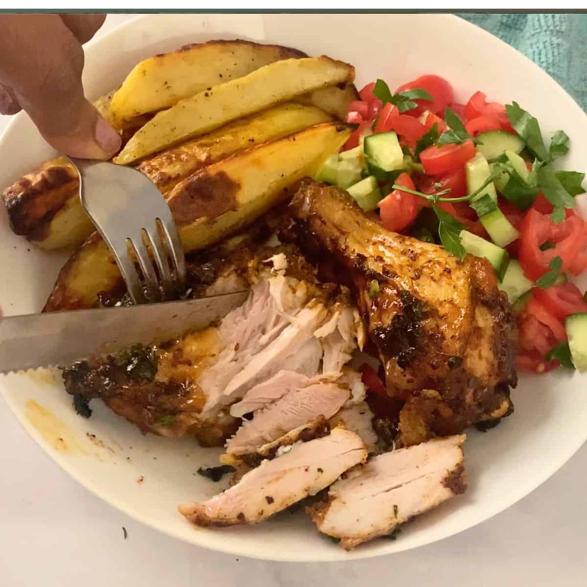 Cutting up the cajun baked chicken on a plate.