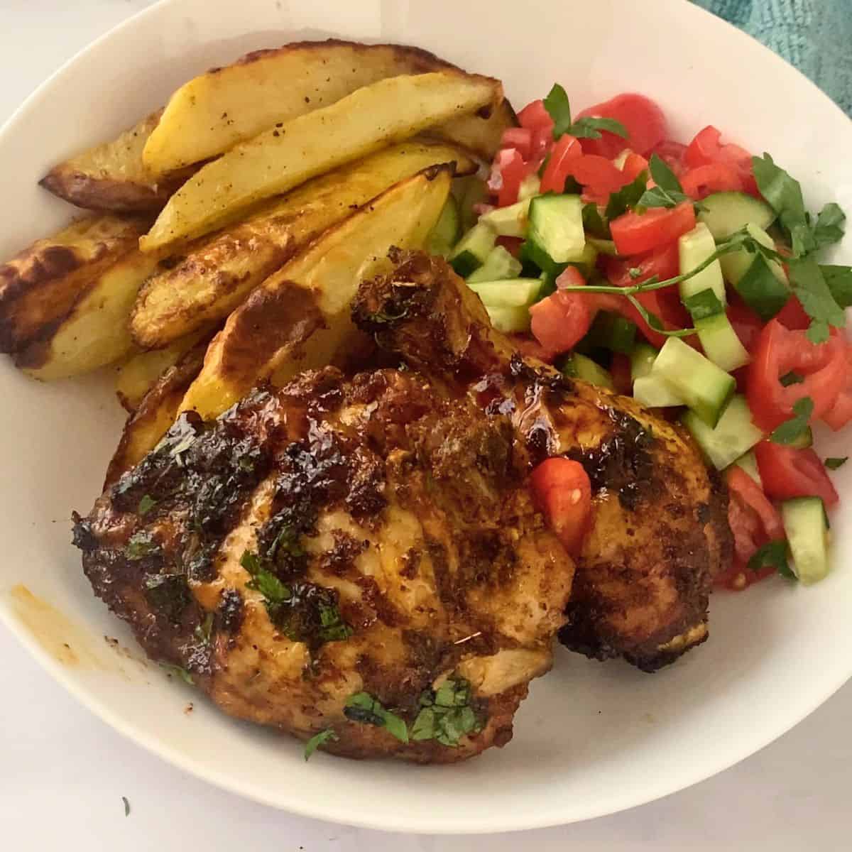 A white plate with salad, cajun chicken and potato fries.