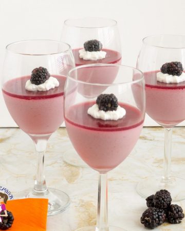 4 wine glasses filled with blackberry Panna Cotta on a table.