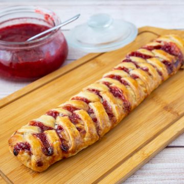 A braided puff pastry with strawberries on a cutting board.
