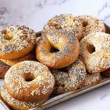 A baking tray with variety of bagels with different toppings.
