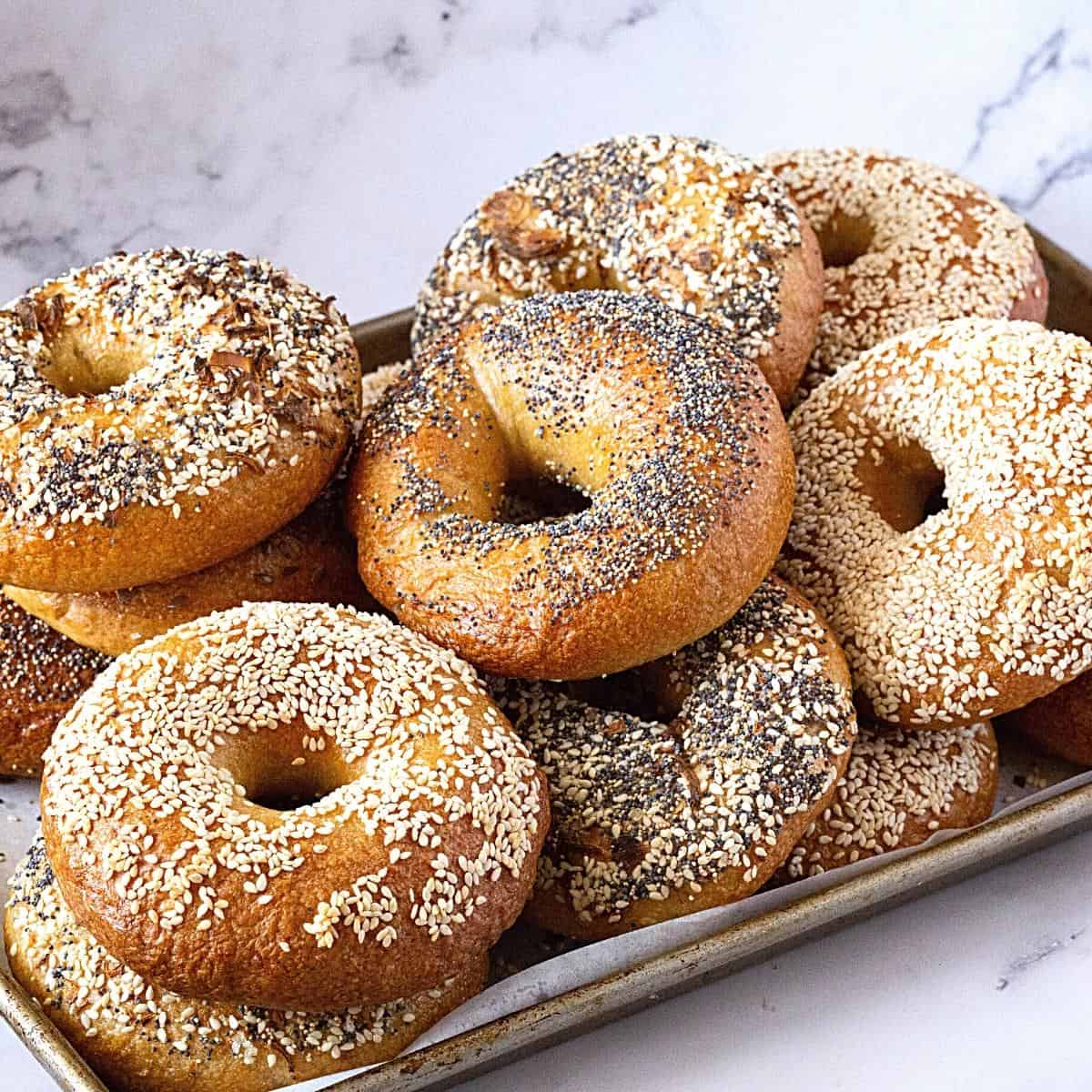 A baking tray with a variety of bagels topped with different toppings.