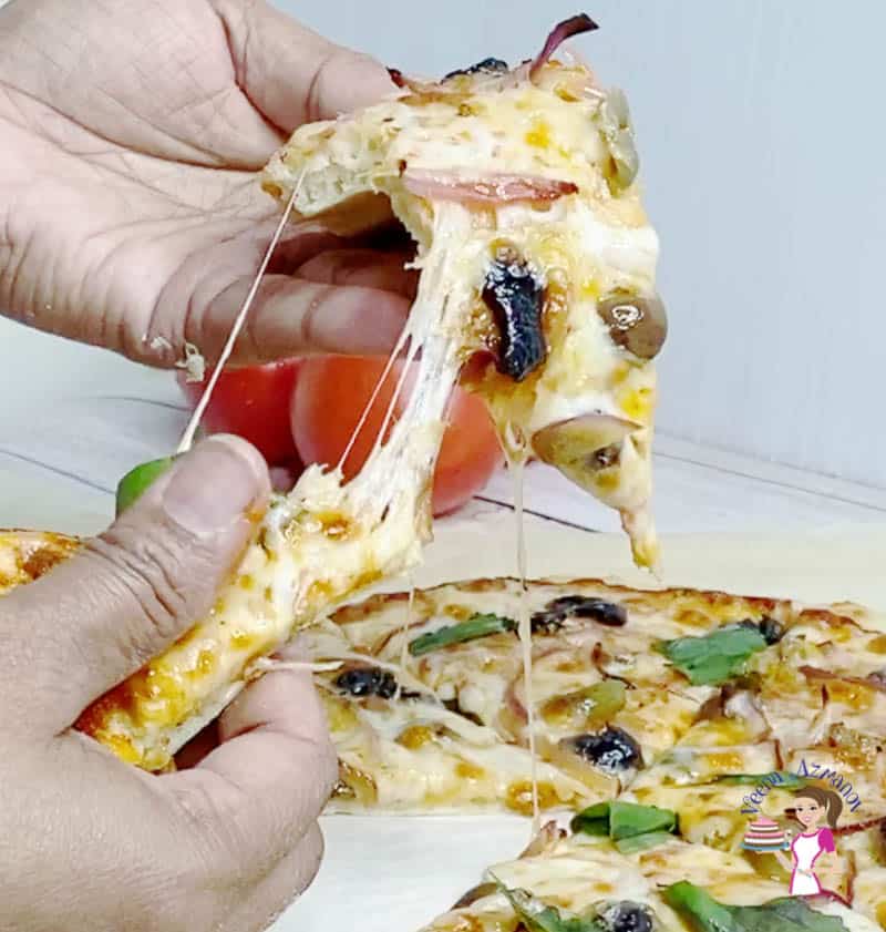 A person holding a slice of pizza with olives and onions.