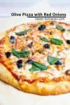 A pizza with olives and onions sitting on top of a wooden board.