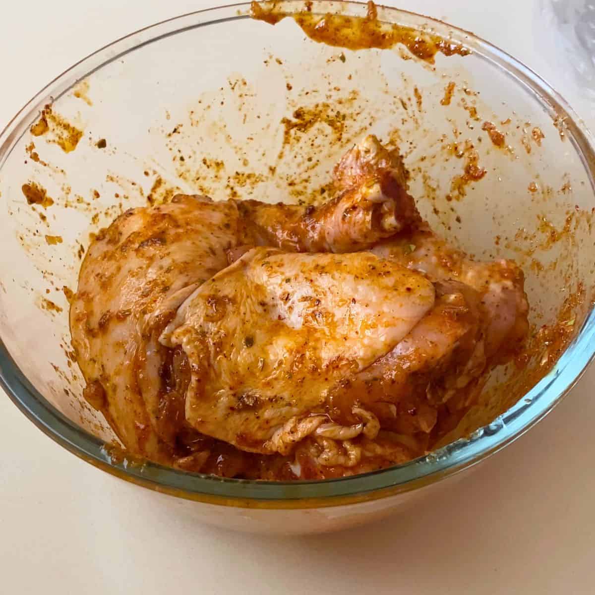 A glass bowl with marinated cajun chicken.
