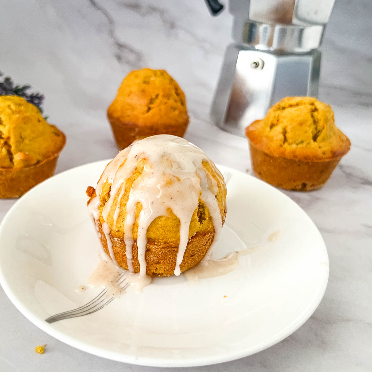 A glazed carrot cake muffin on a plate.