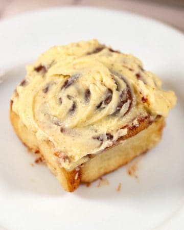 A plate with a cinnabon roll frosted with cream cheese.