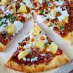 A slice of pineapple pizza on a wooden tray.