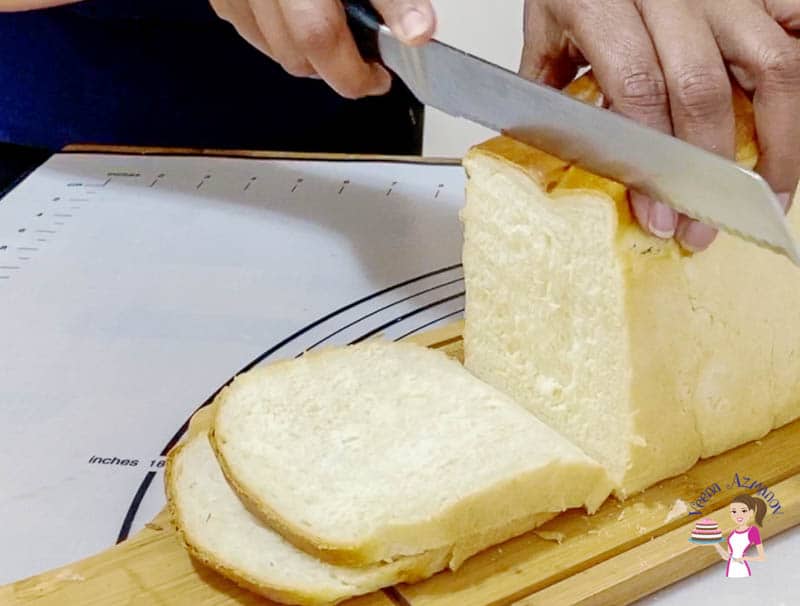 A person slicing a loaf of sandwich bread on a wooden cutting board.