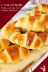 A stack of soft crescent rolls on a wooden tray.