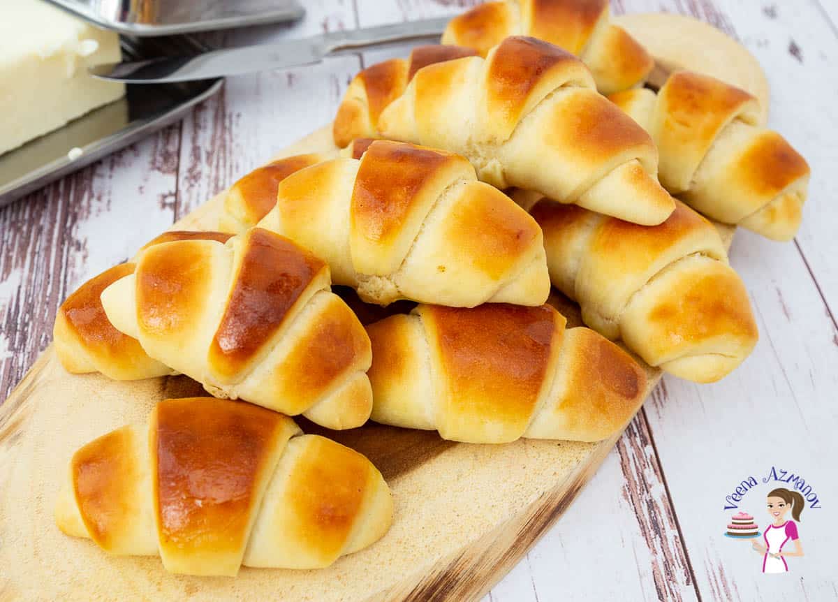 A stack of soft crescent rolls on a wooden tray.