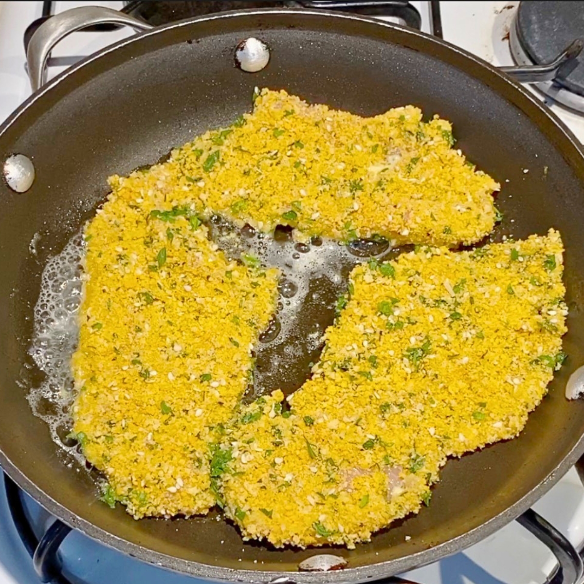 Breaded chicken breast cooking in a skillet.