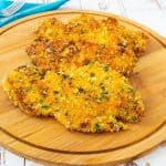 Pan fried breaded chicken breast on a wooden board.