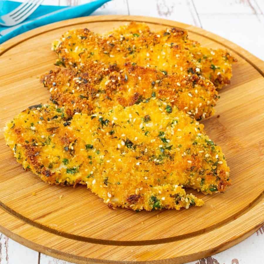 Pan fried breaded chicken breast on a wooden board.