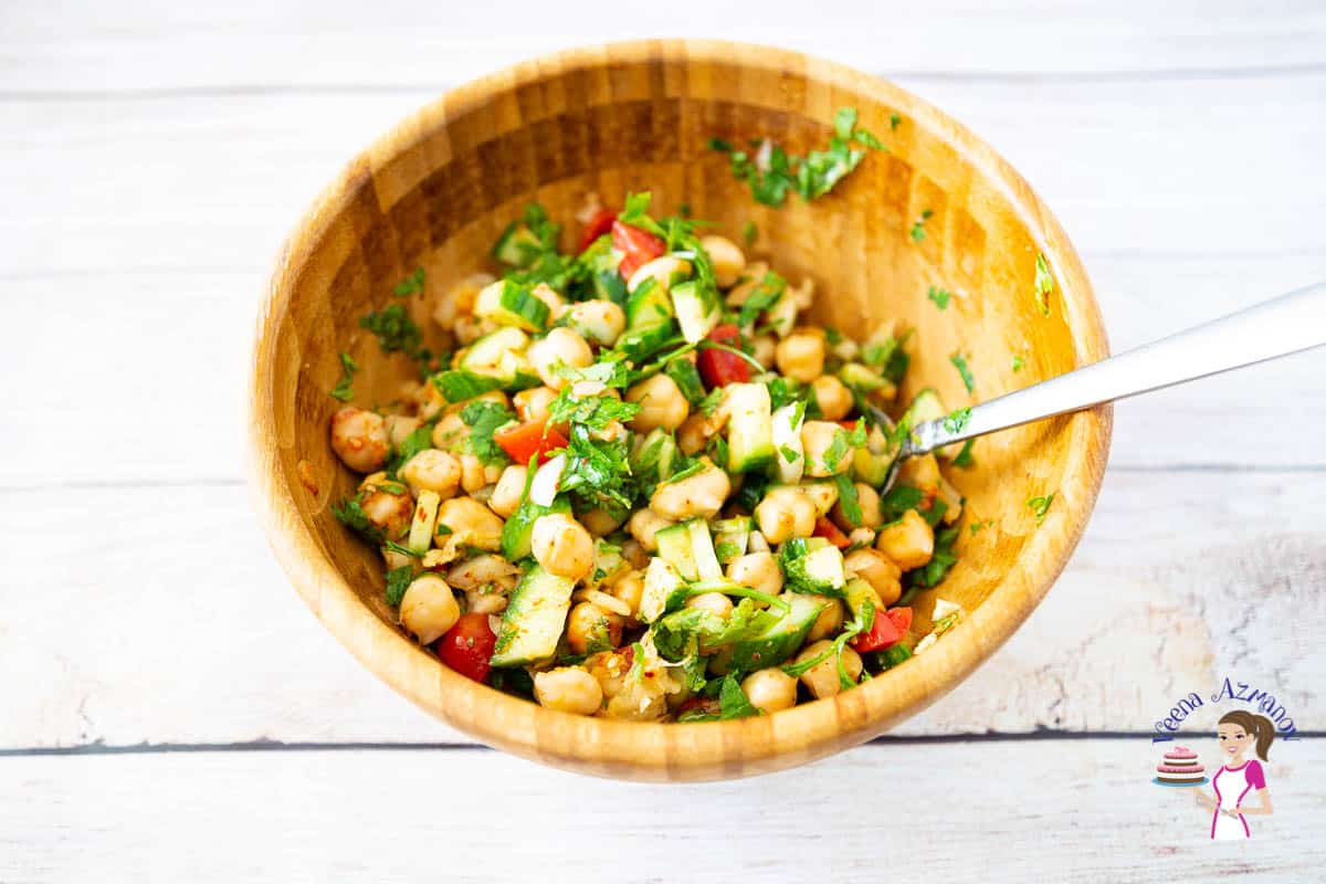 A wooden bowl with chickpeas, cucumbers and Tomato salad.
