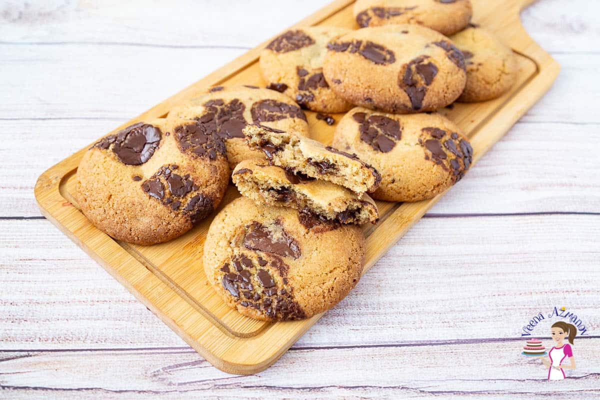 A stack of cookies with chocolate chunks on a wooden board.