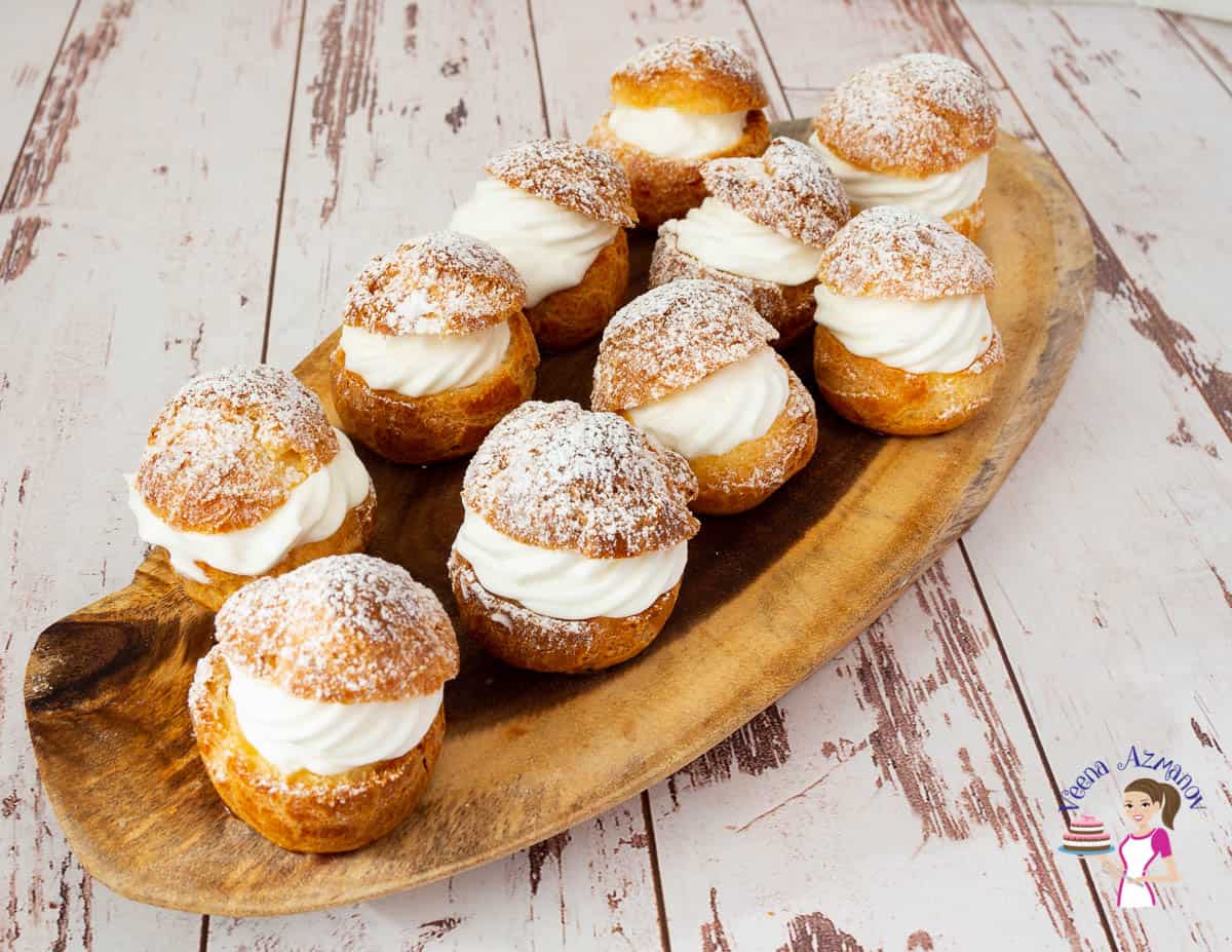 several cream puffs arranged on a wooden tray.