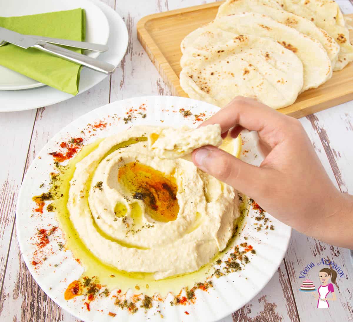 A person eating from a plate of hummus on a table.