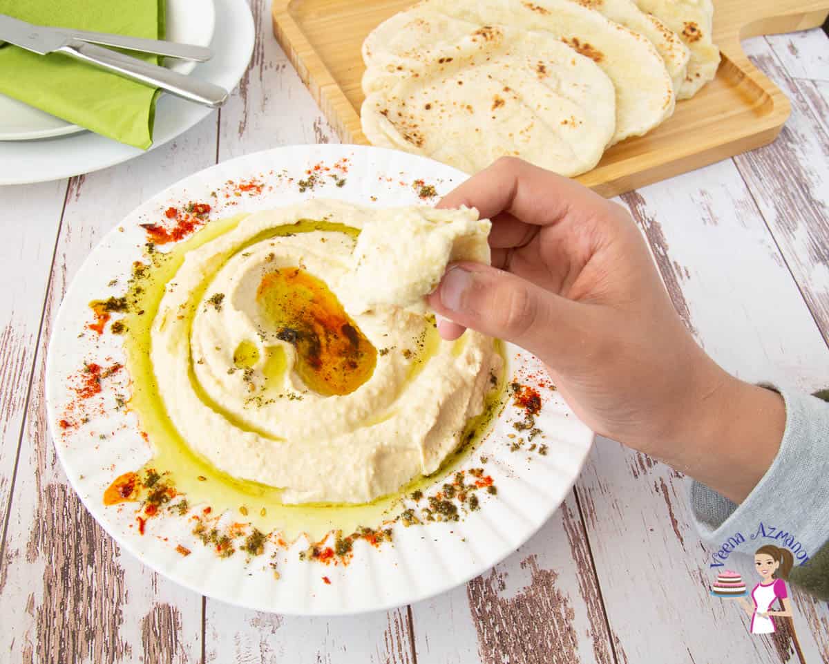 A person eating from a  plate of hummus on a table.