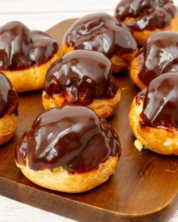 Chocolate glazed profiteroles on a wooden board.