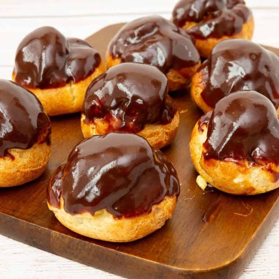 Chocolate glazed profiteroles on a wooden board.