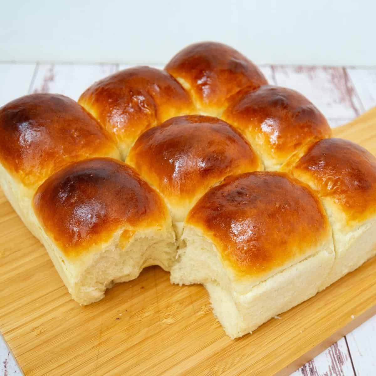 A wooden board with dinner rolls.
