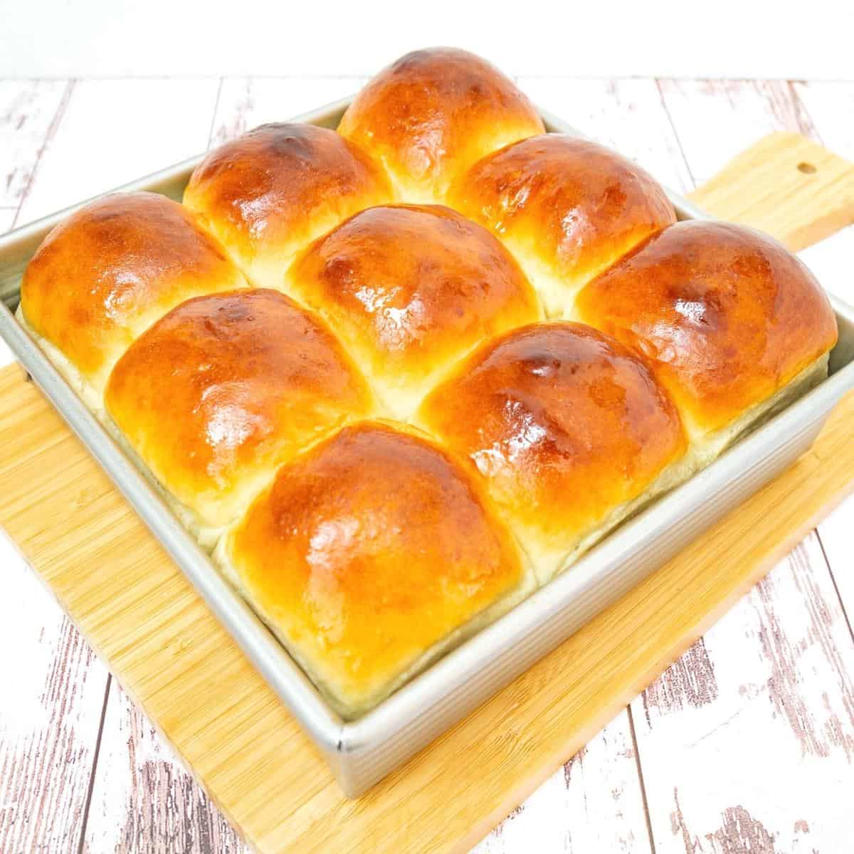 A wooden board with dinner rolls.