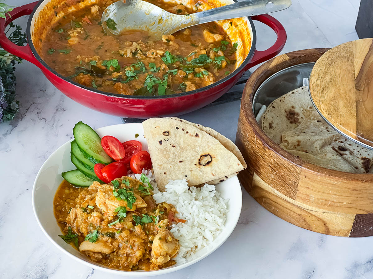 A plate with chicken and lentils with rice and chapati.