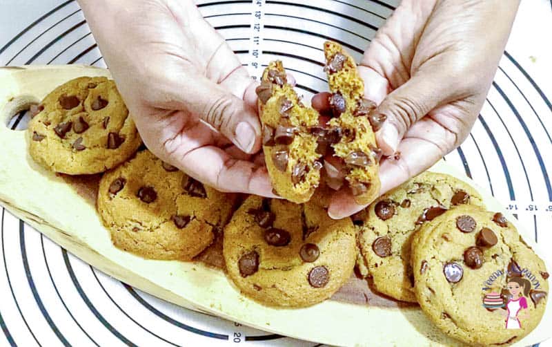 A person breaking in half a chocolate chip cookie.