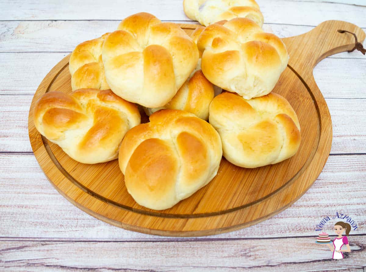 A stack of  dinner rolls on a wooden plate.