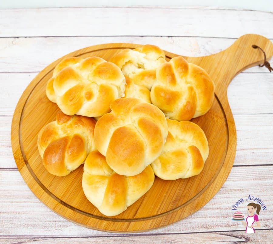 A stack of knotted dinner rolls on a wooden plate.