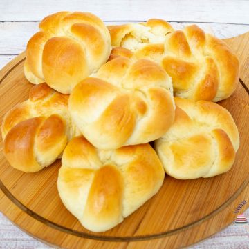 A stack of dinner rolls on a wooden plate.