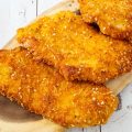 3 Parmesan crusted chicken breasts on a wooden board.