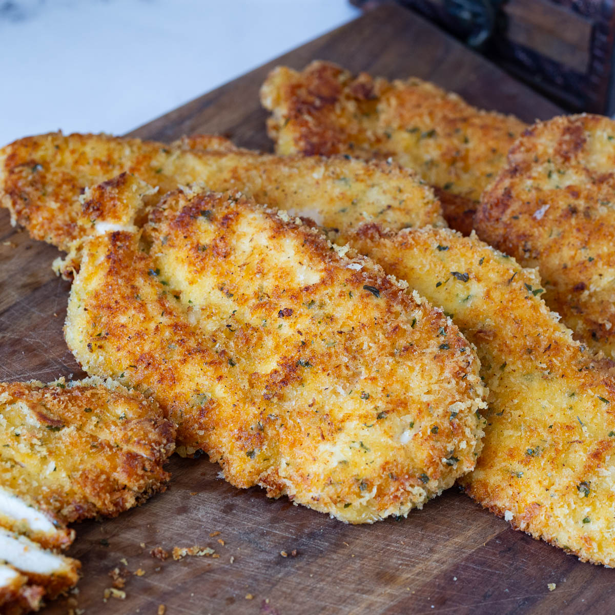 Pan fried chicken crusted with parmesan and breadcrumbs on a board.