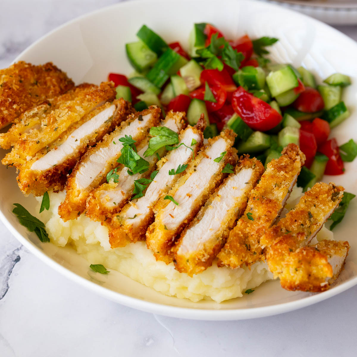 Sliced Parmesan crusted chicken over mashed potatoes.