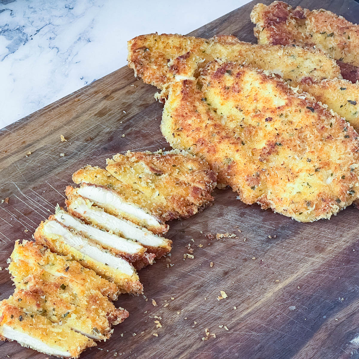A cutting board with sliced chicken parmesan breast.
