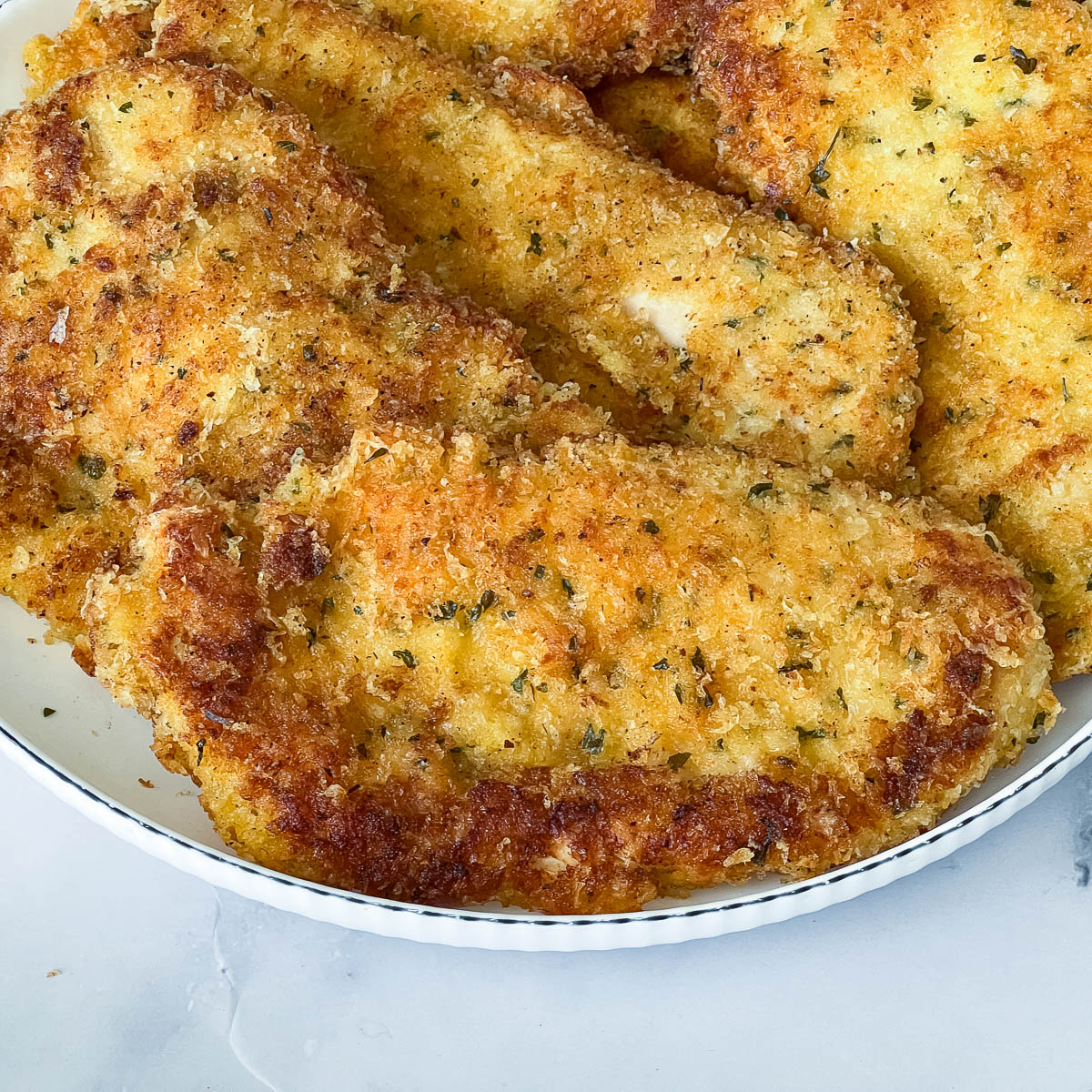 Pan fried chicken parmesan breast on a white plate.