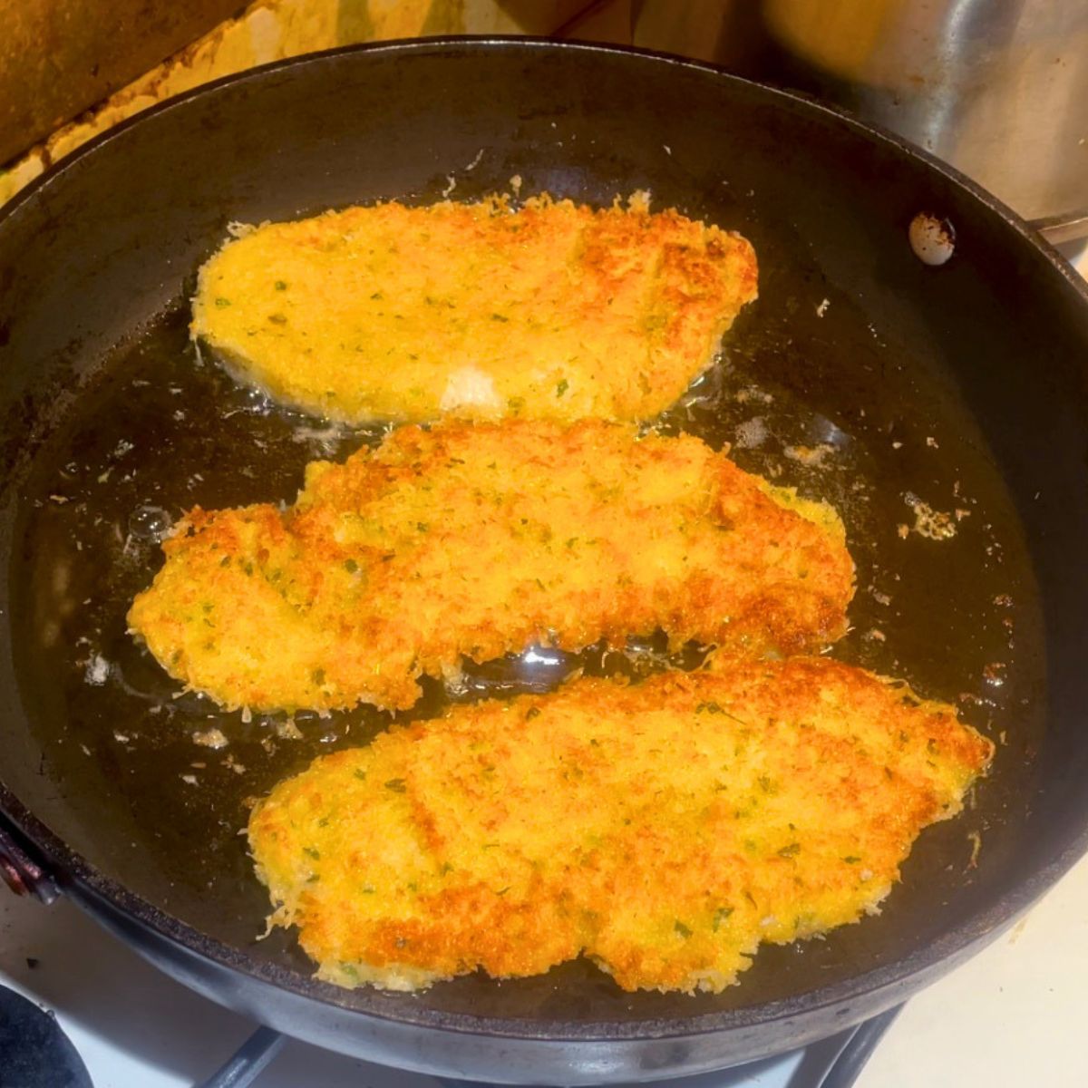 Cooking parmesan chicken breast in a skillet.