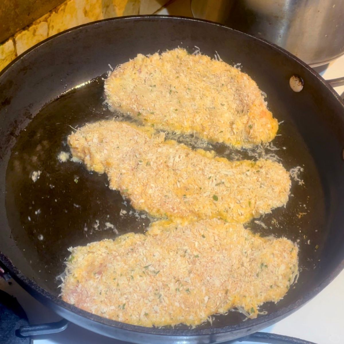 A skillet cooking Parmesan chicken cutlets.