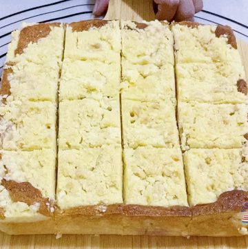 A slices coffee cake with peaches on a wooden board.