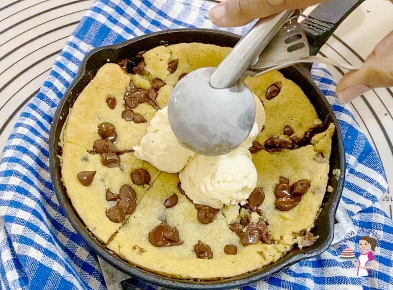 A giant chocolate chip cookie in a skillet, with ice cream on top.